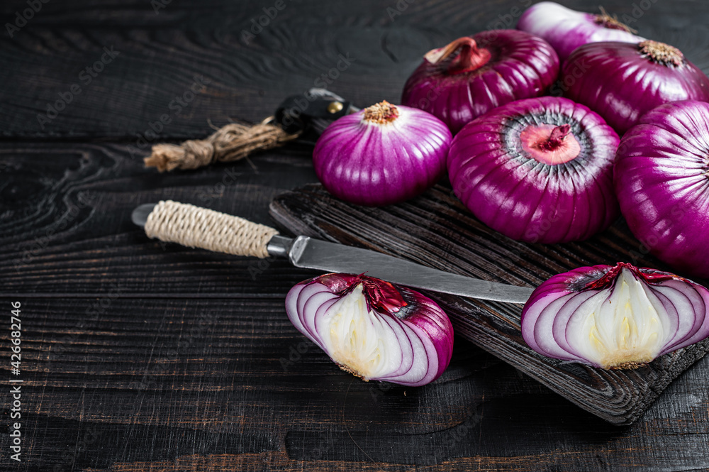 Whole and halfed Flat red sweet onion on a cutting board. Black Wooden background. Top View. Copy space