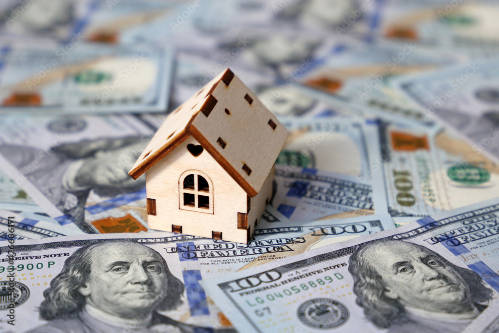 Wooden house model on background of US dollars banknotes. Housing market, purchase or rental of real estate