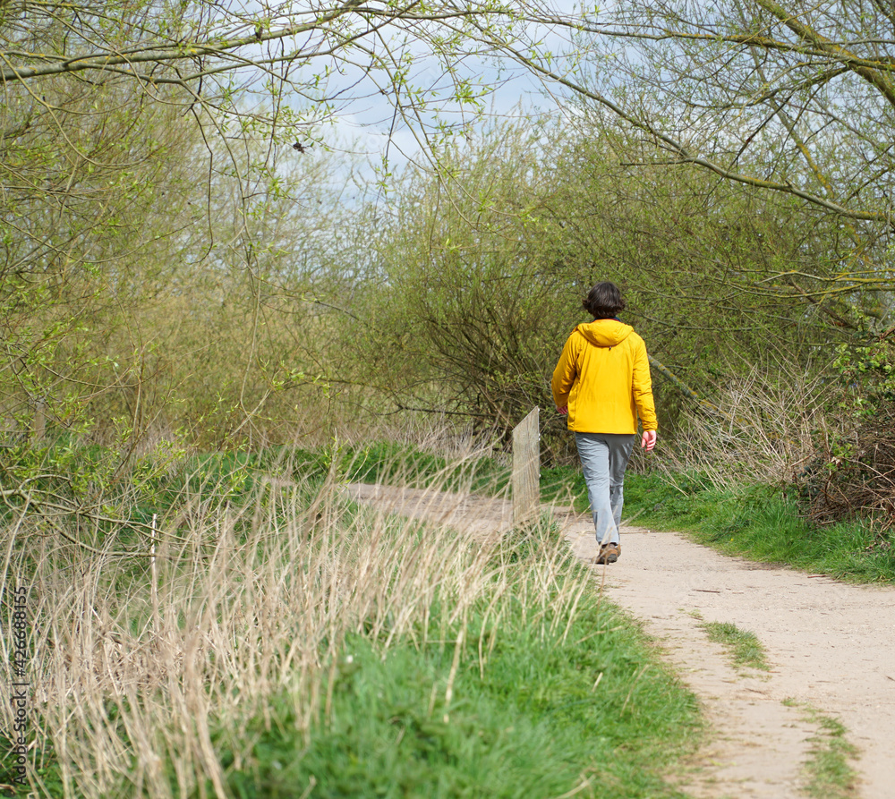 Man wearing yellow coat walking away on a dirt footpath Man wearing yellow coat walking away on a dirt footpath