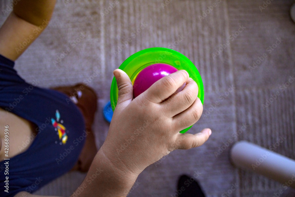 Naklejka premium Top view close up image of a toddler's right hand releasing a purple ball into a green plastic toy with a white carpet on the floor.
