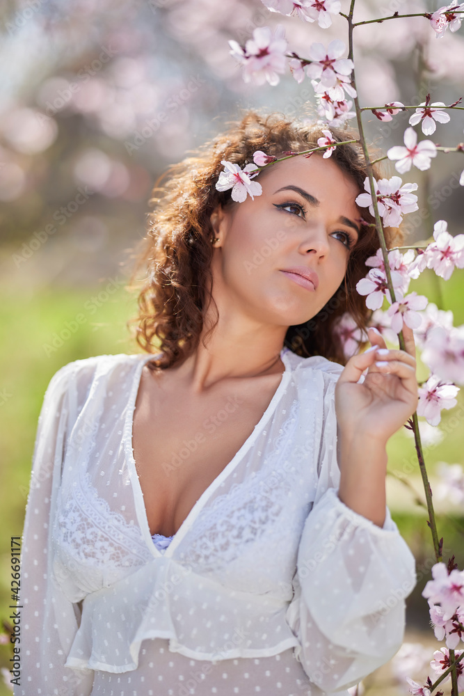spring portrait of a beautiful woman with curly hair next to tree flowers spring portrait of a beautiful woman with curly hair next to tree flowers