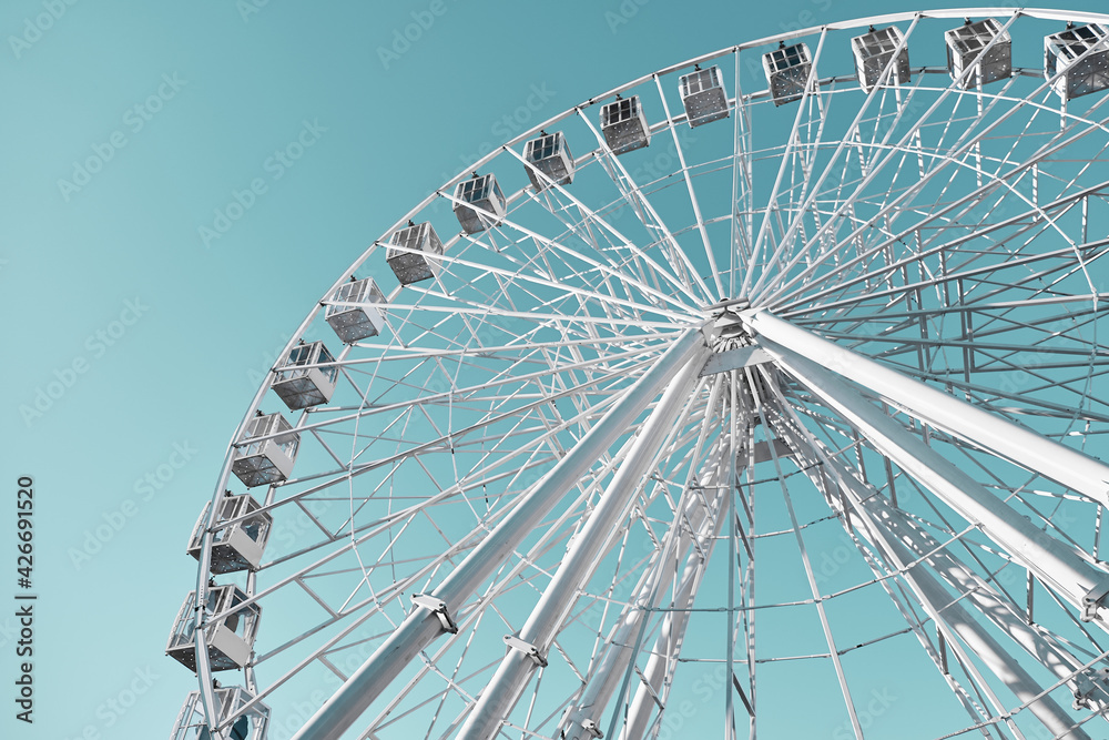 Ferris wheel on a background of turquoise sky. White ferris wheel on a sunny day. Ferris wheel on a background of turquoise sky. White ferris wheel on a sunny day.