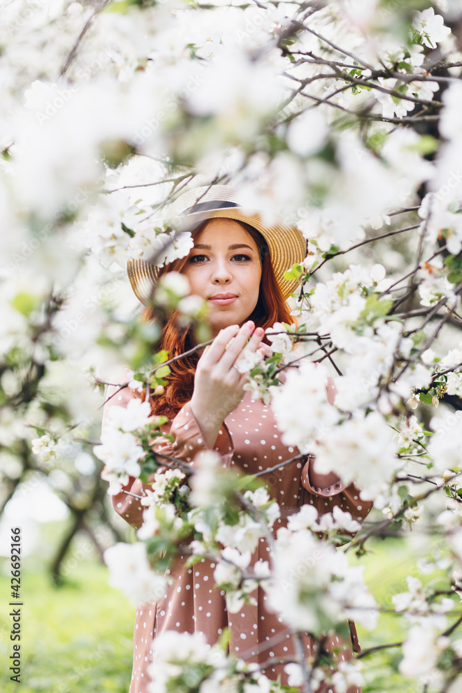 Red-haired girl walks in a spring blooming apple orchard Red-haired girl walks in a spring blooming apple orchard