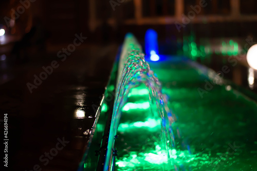 Water jets with blurred focus illuminated by a green lantern at night.