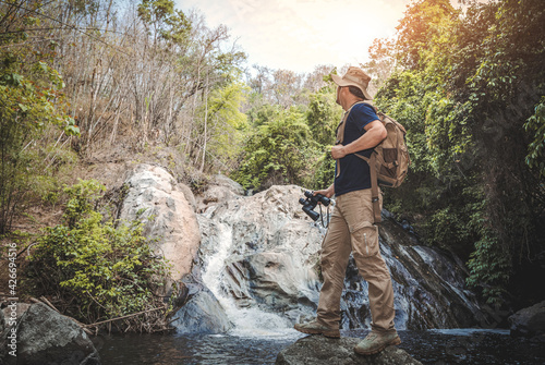 Male hiker with backpack holding binoculars looking waterfall in forest