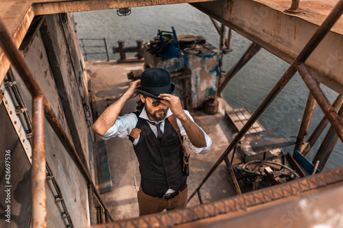 Steampunk. A hero on a river barge surrounded by steel mechanisms. A man with a weapon.