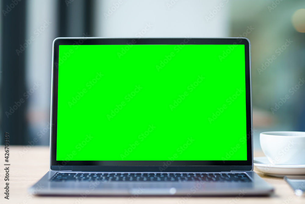 Mockup of laptop computer with empty screen with coffee cup and smartphone on table of the coffee shop background,Green screen