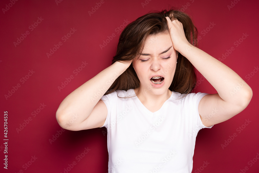 Pretty girl gets annoyed with headache after getting braces. Isolated on red background Pretty girl gets annoyed with headache after getting braces. Isolated on red background