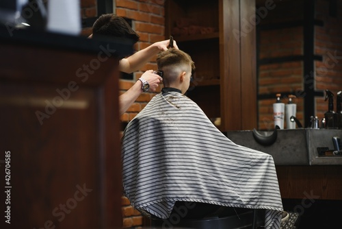 Side view of cute little boy getting haircut by hairdresser at the barbershop