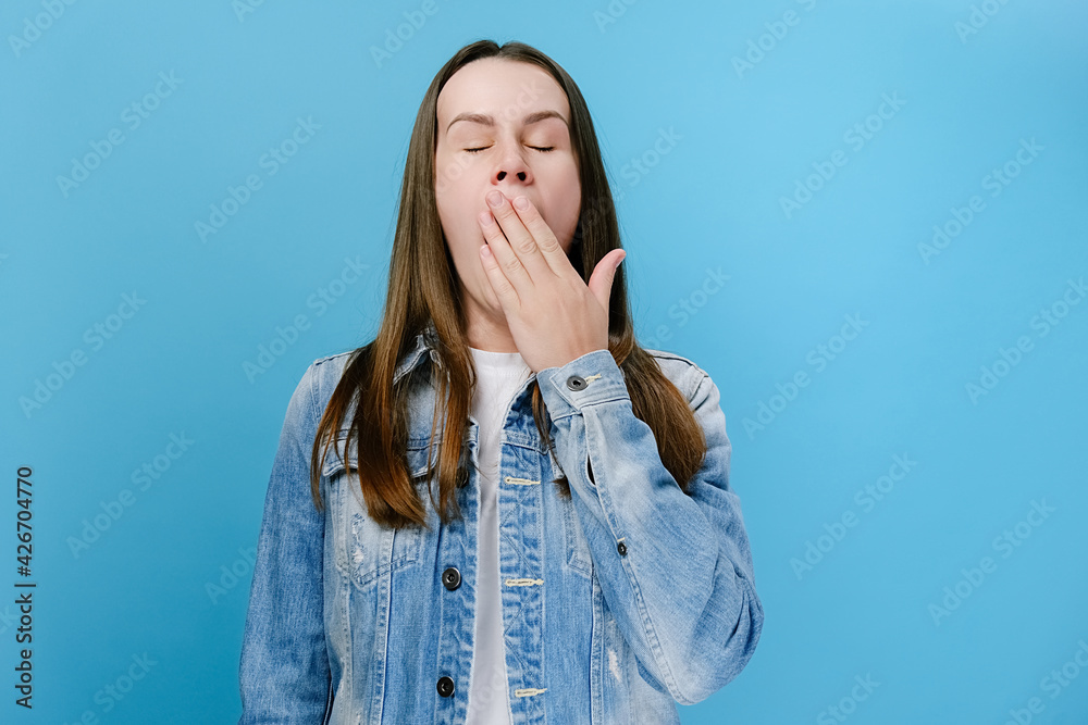 Drowsy girl yawning, sleepy inattentive, feeling somnolent lazy bored gaping suffering from lack of sleep, dressed in denim jacket, isolated on blue studio background. Tiredness and awakening concept Drowsy girl yawning, sleepy inattentive, feeling somnolent lazy bored gaping suffering from lack of sleep, dressed in denim jacket, isolated on blue studio background. Tiredness and awakening concept