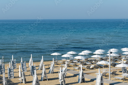 Fototapeta Naklejka Na Ścianę i Meble -  In the morning umbrellas on the beach of Lido di San Pietro in Bevagna near Manduria, regione of Puglia, Italy on a blue Ionian sea background