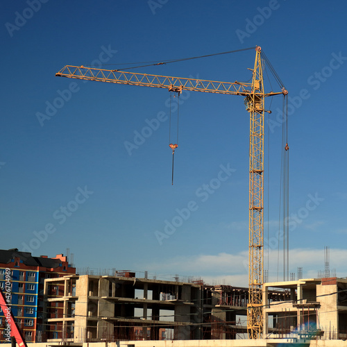 An image of a tower crane against the background of a house under construction.