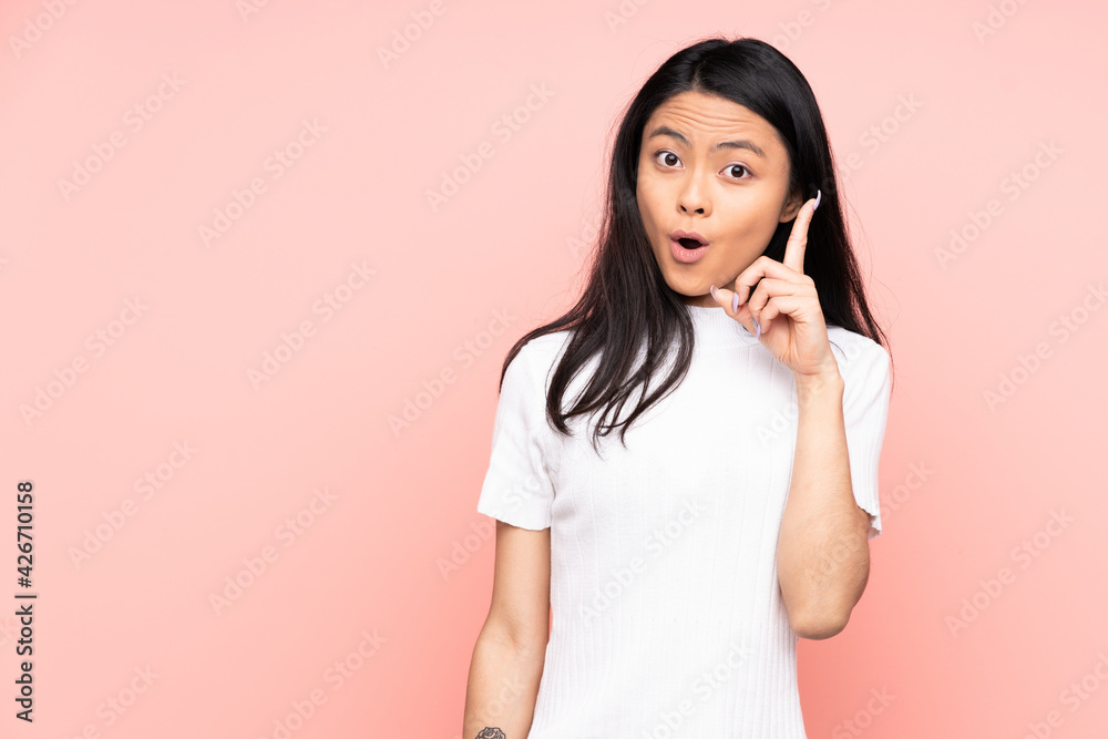 Teenager Chinese woman isolated on pink background intending to realizes the solution while lifting a finger up Teenager Chinese woman isolated on pink background intending to realizes the solution while lifting a finger up