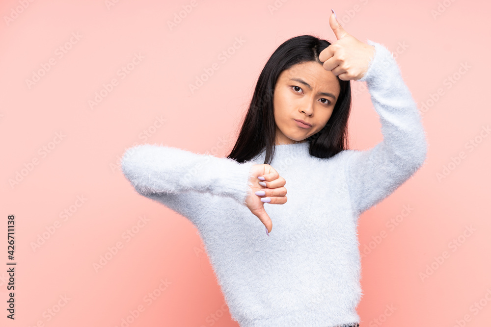 Teenager Chinese woman isolated on pink background making good-bad sign. Undecided between yes or not Teenager Chinese woman isolated on pink background making good-bad sign. Undecided between yes or not