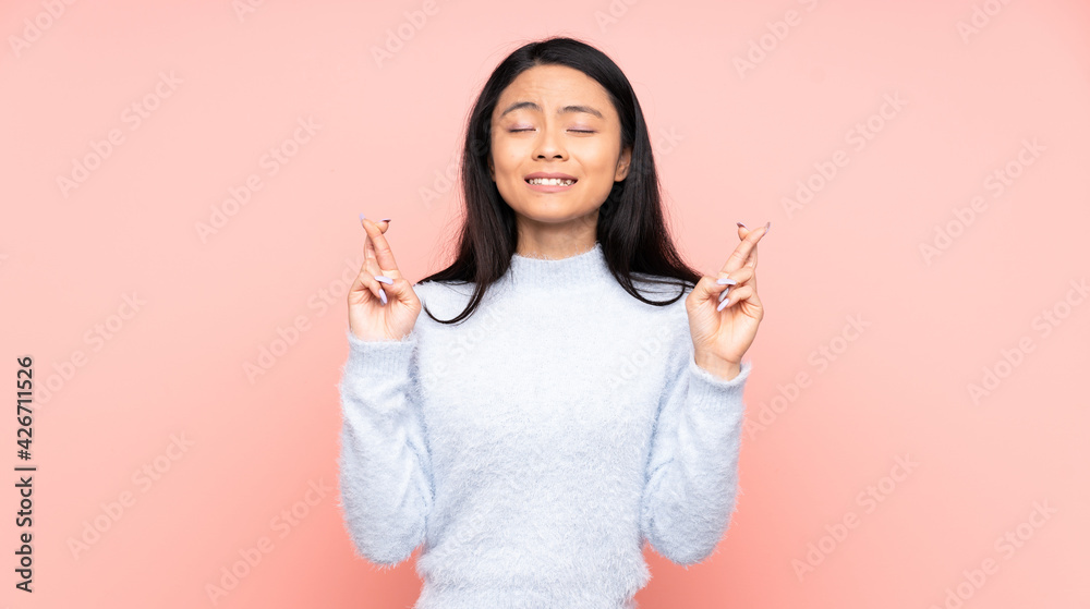 Teenager Chinese woman isolated on pink background with fingers crossing and wishing the best Teenager Chinese woman isolated on pink background with fingers crossing and wishing the best