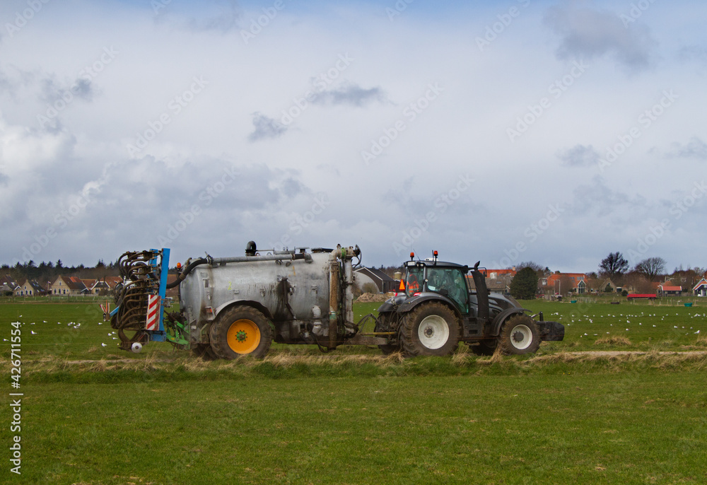 Tractor with slurry tank and slurry injector, in the background a village Tractor with slurry tank and slurry injector, in the background a village