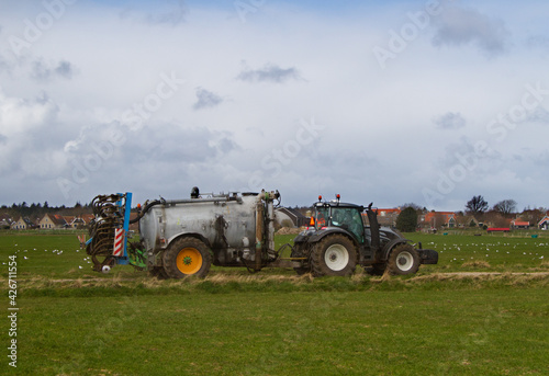 Tractor with slurry tank and slurry injector  in the background a village