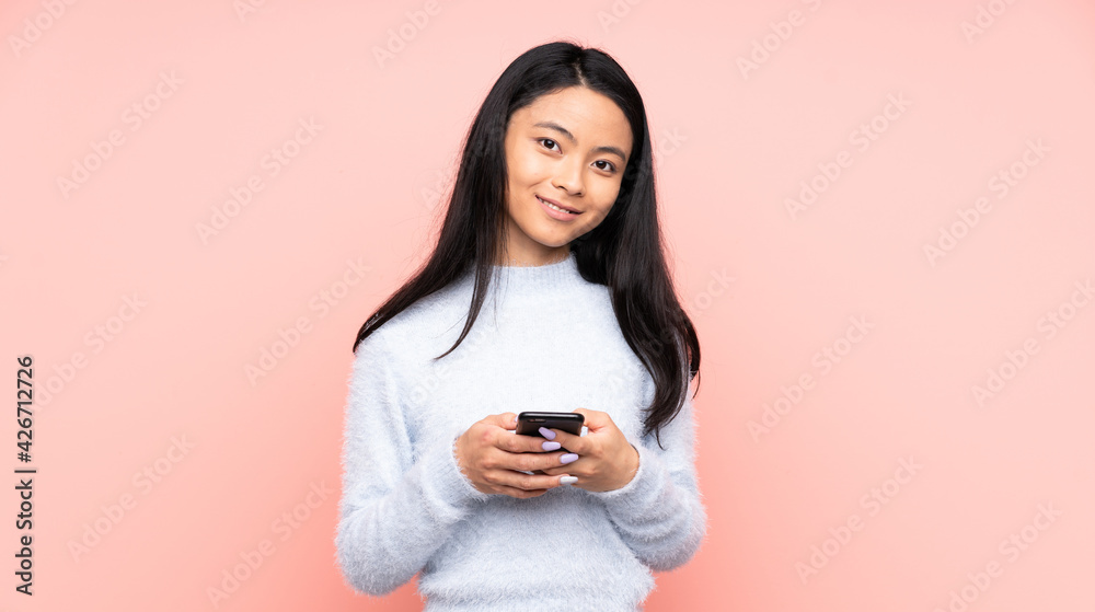 Teenager Chinese woman isolated on pink background sending a message with the mobile Teenager Chinese woman isolated on pink background sending a message with the mobile