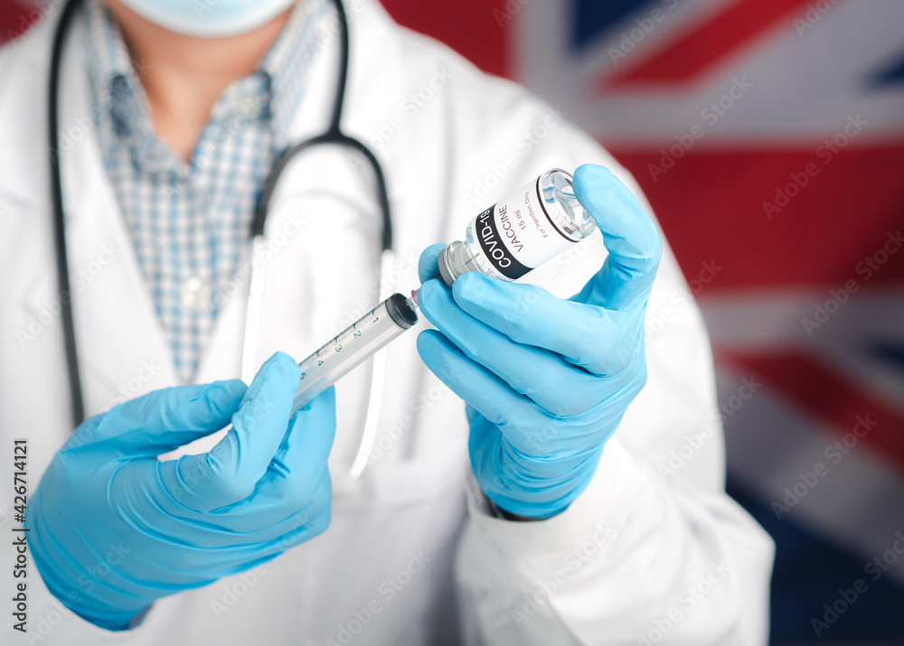 A doctor holding a vaccine bottle and syringe with an England flag background. Vaccine for immunization, and treatment from virus infection. Concept of medical and the fight against the virus A doctor holding a vaccine bottle and syringe with an England flag background. Vaccine for immunization, and treatment from virus infection. Concept of medical and the fight against the virus