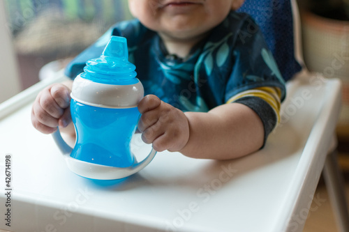 Toddler grasping handles of a sippy cup; learning to use a cup to drink water photo