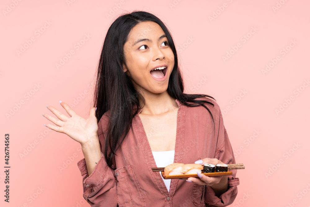 Teenager Asian girl eating sushi isolated on pink background with surprise facial expression Teenager Asian girl eating sushi isolated on pink background with surprise facial expression