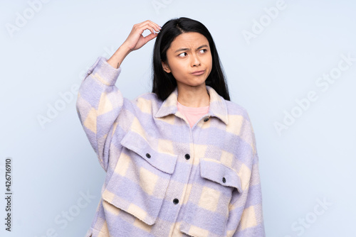 Teenager Chinese woman isolated on blue background having doubts while scratching head © luismolinero