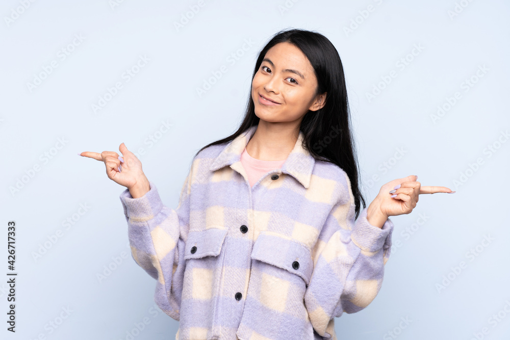 Teenager Chinese woman isolated on blue background pointing finger to the laterals and happy Teenager Chinese woman isolated on blue background pointing finger to the laterals and happy