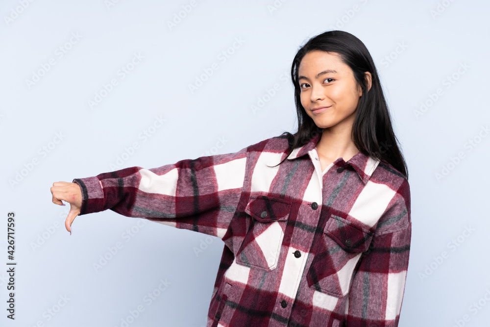 Teenager Chinese woman isolated on blue background showing thumb down with negative expression Teenager Chinese woman isolated on blue background showing thumb down with negative expression
