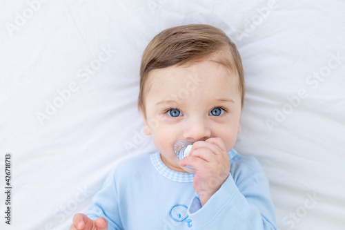 baby boy with pacifier on bed before going to bed in blue bodysuit, happy healthy little baby photo