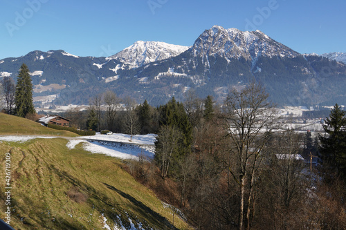 Winteruntypisches Bergpanorama in den Allgäuer Alpen mit grünen Talflanken und Schnee nur auf den Gipfeln