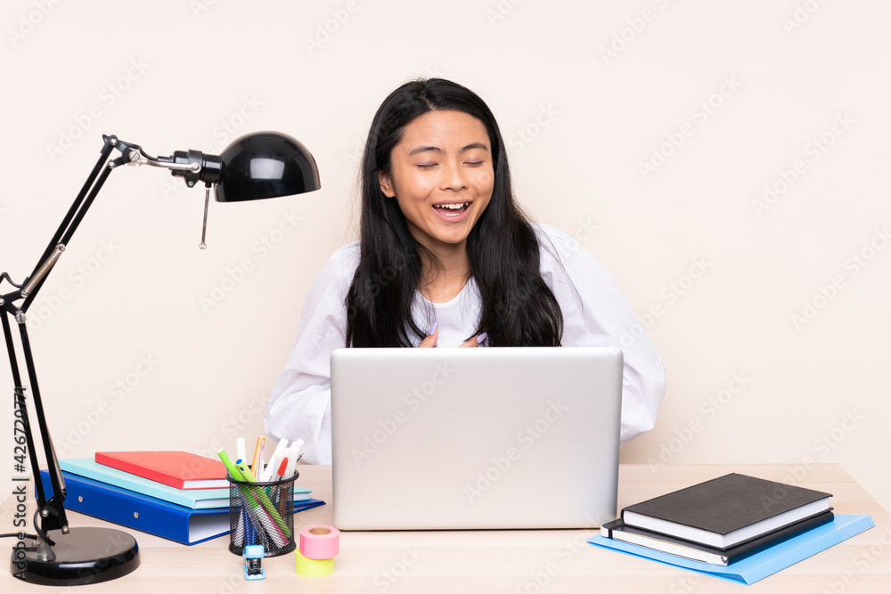 Student asian girl in a workplace with a laptop isolated on beige background smiling a lot Student asian girl in a workplace with a laptop isolated on beige background smiling a lot