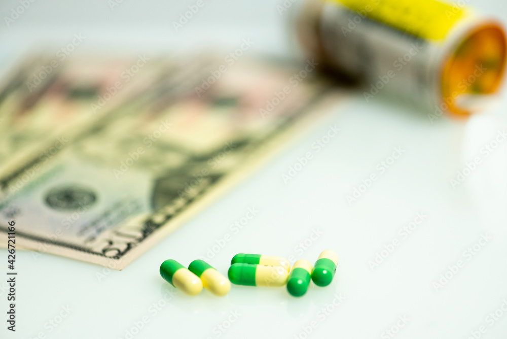 image of prescription capsule, tablets with US cash, currency intentional out of focus in background and bottle of pills. Medical concept. image of prescription capsule, tablets with US cash, currency intentional out of focus in background and bottle of pills. Medical concept.