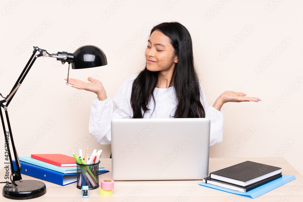 Student asian girl in a workplace with a laptop isolated on beige background holding copyspace with two hands Student asian girl in a workplace with a laptop isolated on beige background holding copyspace with two hands