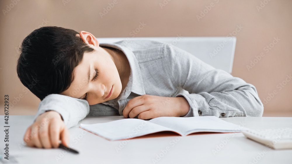 Boy with pen on blurred foreground lying near notebook and calculator on table. Boy with pen on blurred foreground lying near notebook and calculator on table.