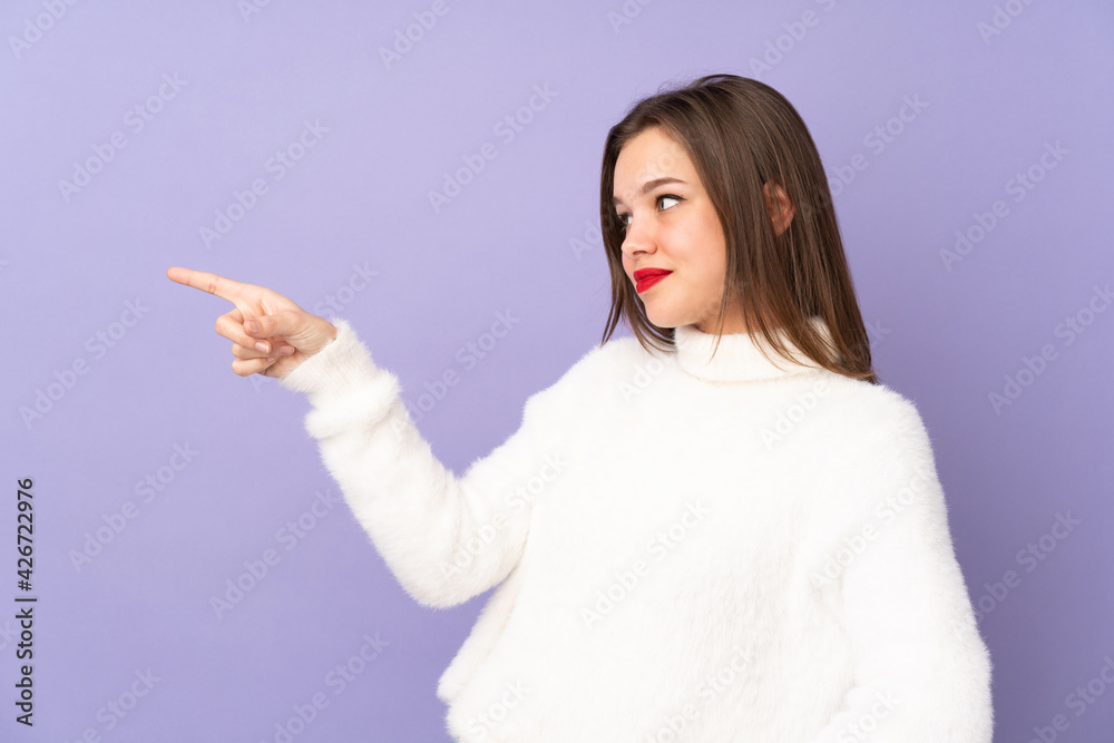 Teenager girl isolated on purple background pointing finger to the side and presenting a product Teenager girl isolated on purple background pointing finger to the side and presenting a product