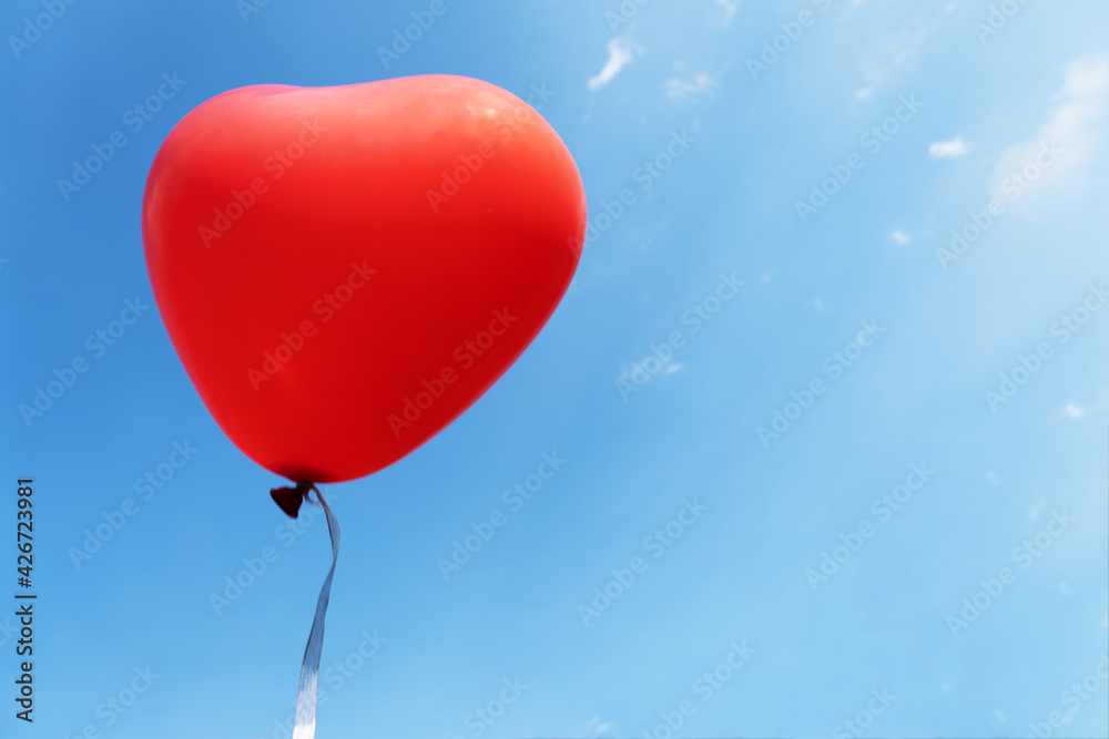 red heart-shaped balloon on blue sky background with clouds