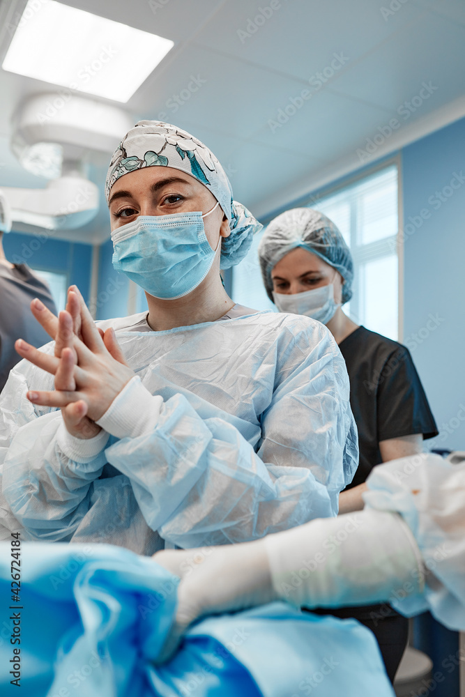 Medical assistant helping a surgeon put on sterile clothes in an operating room . Medical assistant helping a surgeon put on sterile clothes in an operating room .