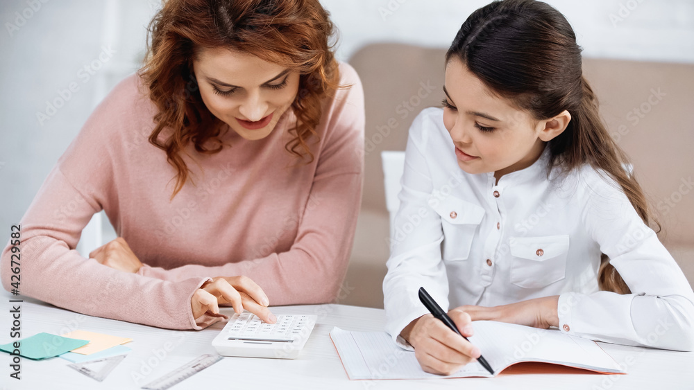 Smiling mother and kid using calculator during homework. Smiling mother and kid using calculator during homework.