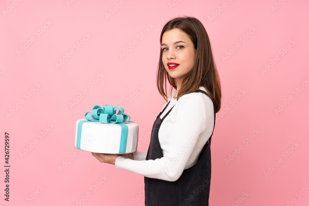 Girl holding a big cake isolated on pink background smiling a lot Girl holding a big cake isolated on pink background smiling a lot