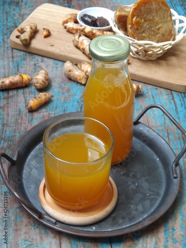 Jamu kunir asem or kunyit asam is Indonesian traditional herbal drink made from turmeric, tamarind, palm sugar. Served on tray with ingredients as background. Better served cold. Healthy refreshment.