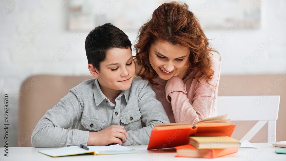 Smiling woman sitting near preteen son and books on blurred foreground. Smiling woman sitting near preteen son and books on blurred foreground.