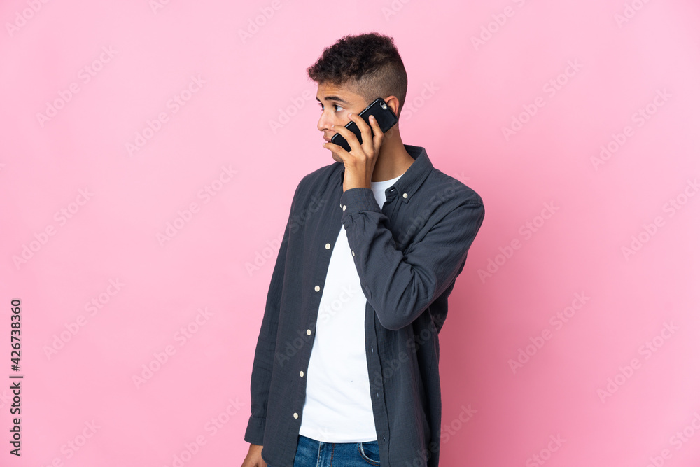 Young Brazilian man isolated on pink background keeping a conversation with the mobile phone with someone Young Brazilian man isolated on pink background keeping a conversation with the mobile phone with someone