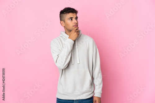 Young Brazilian man isolated on pink background and looking up © luismolinero