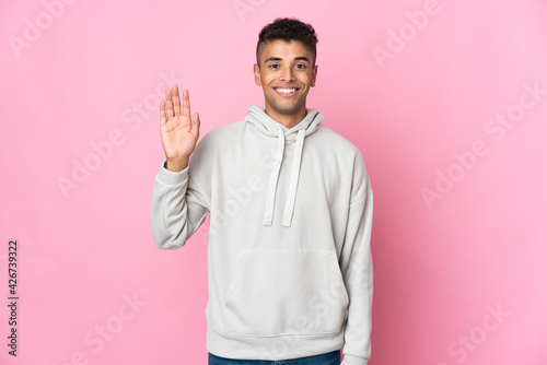 Young Brazilian man isolated on pink background saluting with hand with happy expression © luismolinero