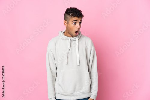 Young Brazilian man isolated on pink background doing surprise gesture while looking to the side