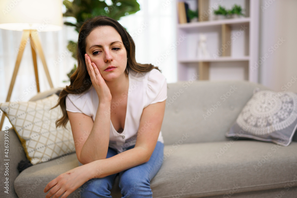 Stressed mature woman sitting on sofa at home look sad Stressed mature woman sitting on sofa at home look sad