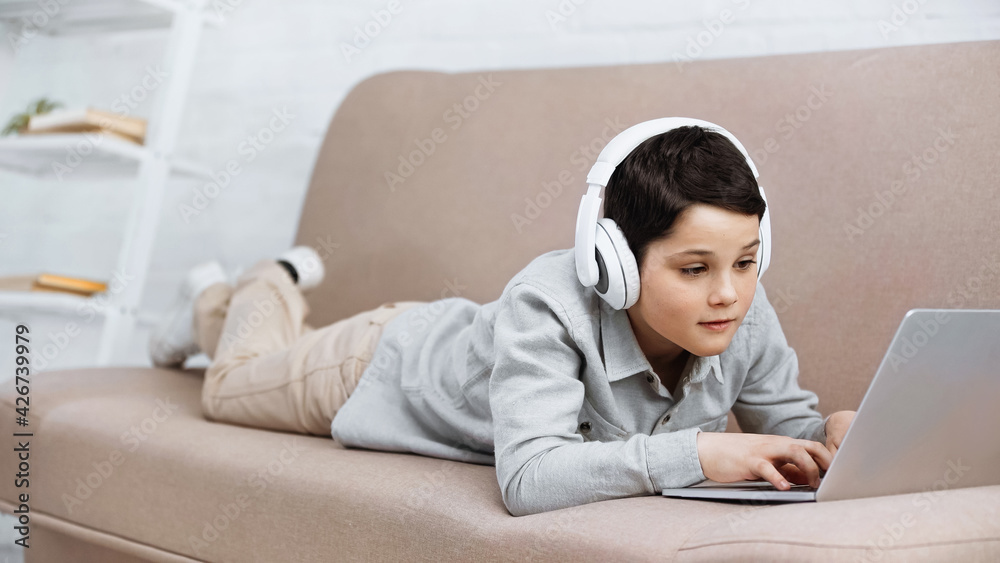 Preteen boy in headphones using laptop on couch. Preteen boy in headphones using laptop on couch.