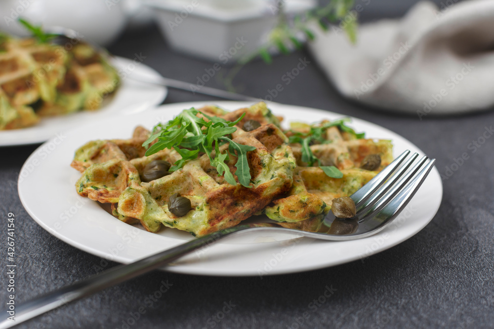zucchini waffles, served with fresh arugula and capers on white plate.