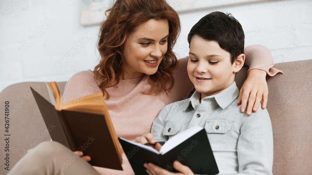 Smiling mother holding book near son with notebook during education at home. Smiling mother holding book near son with notebook during education at home.