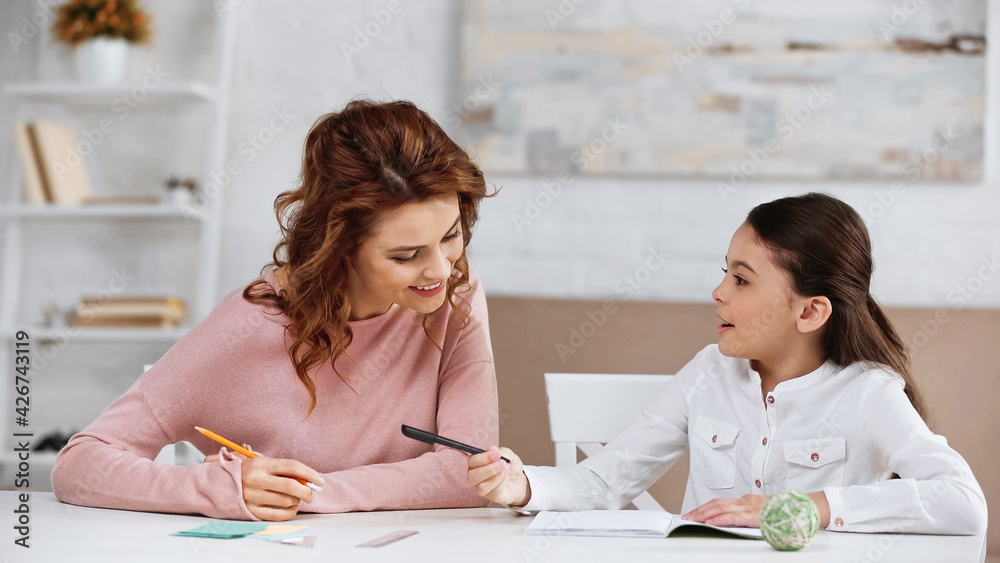 Kid with pen talking to mother near notebook and stationery. Kid with pen talking to mother near notebook and stationery.